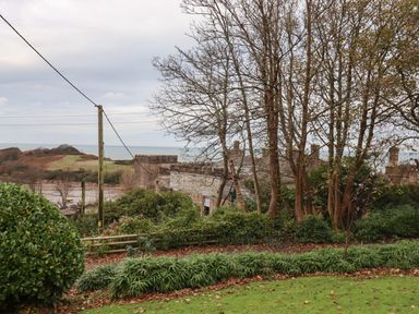 A garden with trees and bushes overlooking a stone building and a body of water at Castle View Lodge in Ilfracombe
