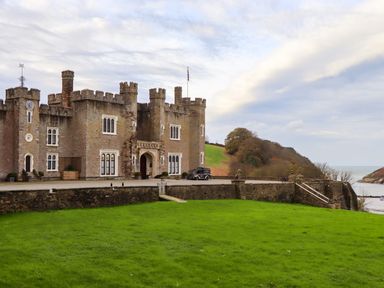 A castle with battlements near a grassy lawn and a view of the sea at Castle View Lodge in Ilfracombe