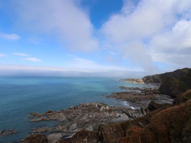 Rocky coastline with cliffs and the sea under a cloudy blue sky at Castle View Lodge in Ilfracombe