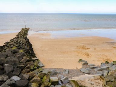 A beach with a rock pier and ocean at Highland House Sheringham