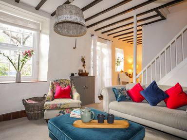 A living room with floral armchair red and blue cushions on a gray sofa wooden beams on ceiling at Riverwash Cottage in Dwygyfylchi