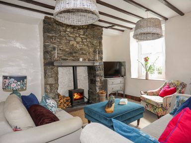 A living room with a stone fireplace and wood burner two sofas an ottoman and a floral armchair with a window at Riverwash Cottage in Dwygyfylchi