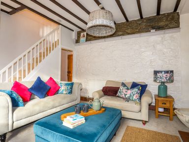 A living room with two sofas and a blue ottoman table with books and a teapot at Riverwash Cottage in Dwygyfylchi