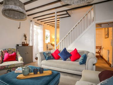 A living room with sofas and colorful cushions a floral armchair a wooden staircase and a coffee table at Riverwash Cottage in Dwygyfylchi