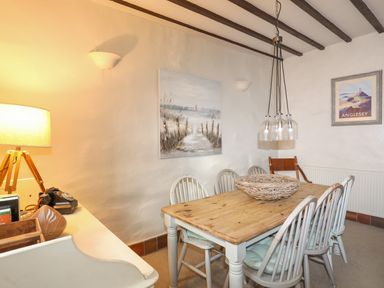 A dining room with a wooden table and six chairs a lamp and paintings on the wall at Riverwash Cottage in Dwygyfylchi