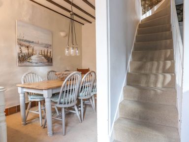 A dining area with wooden table and chairs next to a carpeted staircase at Riverwash Cottage in Dwygyfylchi