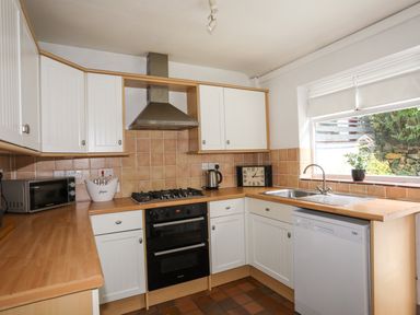 A kitchen with white cabinets a gas stove oven microwave dishwasher sink and a window at Riverwash Cottage in Dwygyfylchi