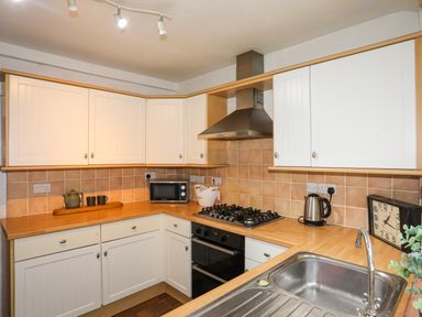 A kitchen with white cabinets a gas stove a microwave a kettle a wall clock and a sink at Riverwash Cottage in Dwygyfylchi