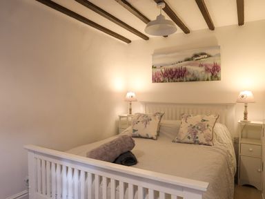 A bedroom with a white bed frame two bedside tables with lamps and a painting above the bed at Riverwash Cottage in Dwygyfylchi