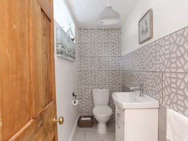 A small bathroom with a white toilet and sink and patterned wall tiles at Riverwash Cottage in Dwygyfylchi