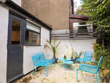An outdoor patio area with blue metal chairs and tables next to a white building with a black door and window at Riverwash Cottage in Dwygyfylchi
