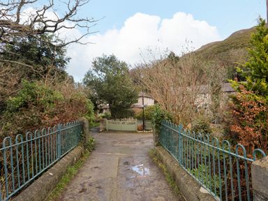 A narrow paved path with blue metal railings on both sides leading to a green wooden gate and houses in the background at Riverwash Cottage in Dwygyfylchi