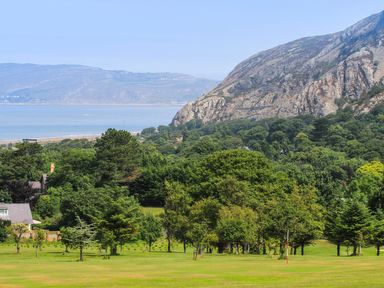A green golf course with trees in front of mountains near a body of water at Riverwash Cottage in Dwygyfylchi