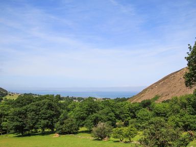 A landscape with green trees and hills and a view of the sea at Riverwash Cottage in Dwygyfylchi