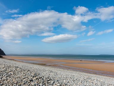A pebble and sandy beach with people near the water under a blue sky at Riverwash Cottage in Dwygyfylchi