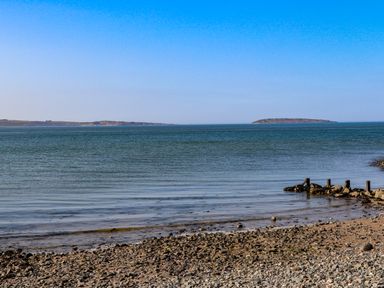 A rocky beach with calm sea and two land masses in the distance at Riverwash Cottage in Dwygyfylchi