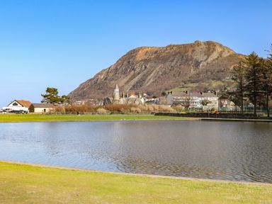 A lake with grass in the foreground houses and a mountain in the background at Riverwash Cottage in Dwygyfylchi
