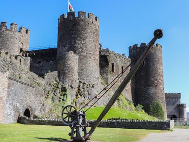 A stone castle with multiple rounded towers and a large old wooden crane in front at Riverwash Cottage in Dwygyfylchi