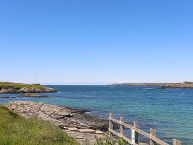 A rocky coastline with steps leading to the water and a grassy area at Seaddler in Trearddur Bay