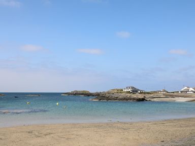 A sandy beach with rocks and houses near the coastline at Seaddler in Trearddur Bay