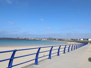 A beachfront promenade with a blue railing along a sandy beach and sea at Seaddler in Trearddur Bay