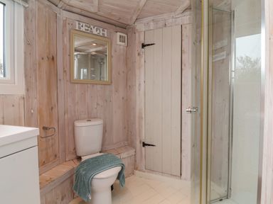 A bathroom with a toilet with a towel on the seat wood paneled walls a shower enclosure a mirror and a cabinet at Shipload Bay near Hartland