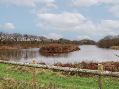A pond surrounded by trees and bushes with a wooden fence in the foreground at Shipload Bay near Hartland