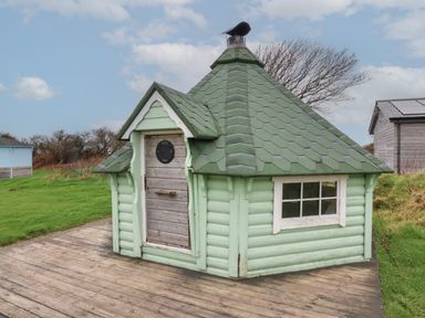 A small green wooden BBQ hut with a shingled roof on a wooden deck near Hartland