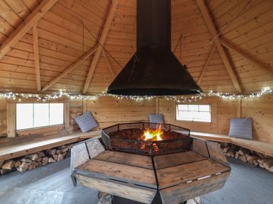 A wooden cabin interior with a central firepit surrounded by benches and pillows at Shipload Bay near Hartland