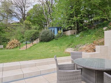 A garden with tiled patio furniture stairs and a small blue shed at Upper Cottage in Rocombe near Uplyme