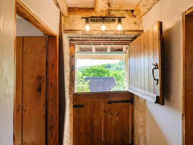 An open stable door with wooden beams and window shutters showing a green landscape outside at Upper Cottage in Rocombe near Uplyme