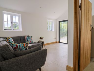 A sitting room with a grey sofa with patterned cushions small side tables with flowers tiled floor and glass door at Upper Cottage in Rocombe near Uplyme