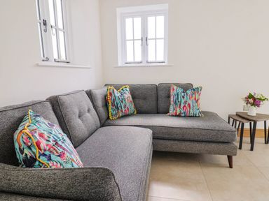A grey sectional sofa with colorful pillows near two small wooden side tables with flowers at Upper Cottage in Rocombe near Uplyme