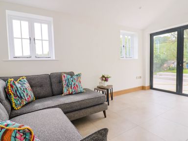 A living room with a gray sofa with colorful cushions flowers on a small table and large glass doors at Upper Cottage in Rocombe near Uplyme