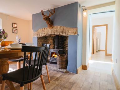 A dining area with a wooden table and black chairs near a fireplace with a wood stove and a wall-mounted deer head at Upper Cottage in Rocombe near Uplyme