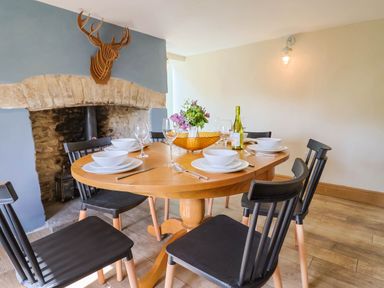 A dining room with a wooden table set for six and a stone fireplace at Upper Cottage in Rocombe near Uplyme