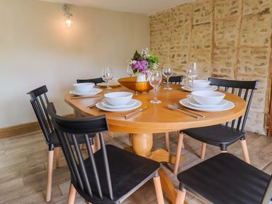 A dining table set with white dishes glasses and cutlery with black chairs around it and a stone wall at Upper Cottage in Rocombe near Uplyme