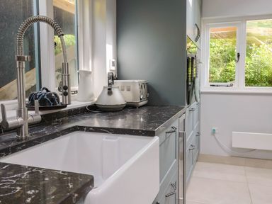 A kitchen countertop with a sink, faucet, kettle, toaster, and ceramic jug near windows at Upper Cottage in Rocombe near Uplyme