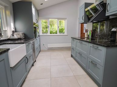 A kitchen with blue cabinets black countertops white tiles and a window showing greenery at Upper Cottage Rocombe near Uplyme