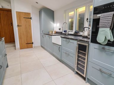 A kitchen with light blue cabinets a white sink a black countertop a wine cooler and wooden doors at Upper Cottage in Rocombe near Uplyme
