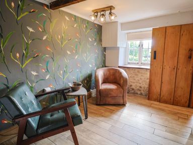 A small room with two chairs a side table floral wallpaper window and wooden cupboard at Upper Cottage Rocombe near Uplyme