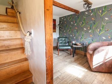 A wooden staircase with a rope handrail next to a room with two chairs a small table and floral wallpaper at Upper Cottage Rocombe near Uplyme