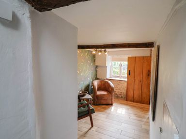 A small sitting area with a brown armchair green patterned wallpaper a wooden window frame and a wooden door at Upper Cottage in Rocombe near Uplyme