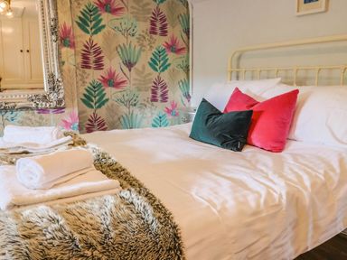 A bed with white sheets red and green pillows and folded white towels on a furry blanket at Upper Cottage in Rocombe near Uplyme