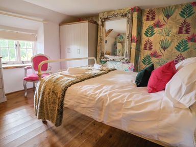 A bedroom with a bed covered in white linens and colorful pillows next to a window and a white wardrobe at Upper Cottage Rocombe near Uplyme