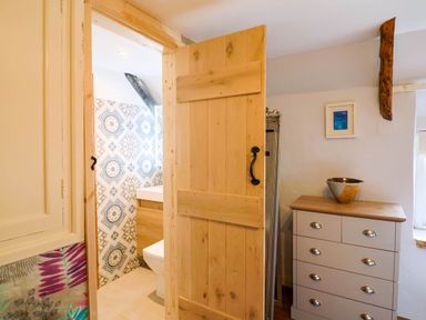 A wooden door open to a bathroom with patterned tiles next to a chest of drawers and a decorative bowl at Upper Cottage Rocombe near Uplyme
