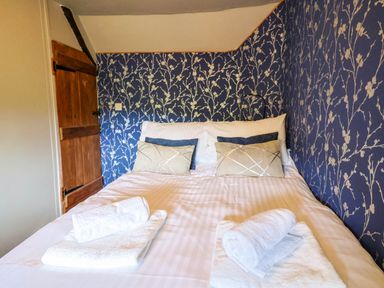 A bed with pillows and rolled towels against a blue floral wallpaper at Upper Cottage in Rocombe near Uplyme