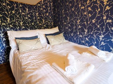 A bedroom with a double bed white striped bedding patterned pillows and floral wallpaper at Upper Cottage in Rocombe near Uplyme