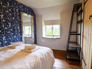 A bedroom with a bed with folded towels a large mirror a window and a shelving unit at Upper Cottage in Rocombe near Uplyme