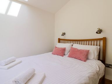 A bedroom with a wooden bed frame white bedding rolled towels and pink cushions at Upper Cottage in Rocombe near Uplyme